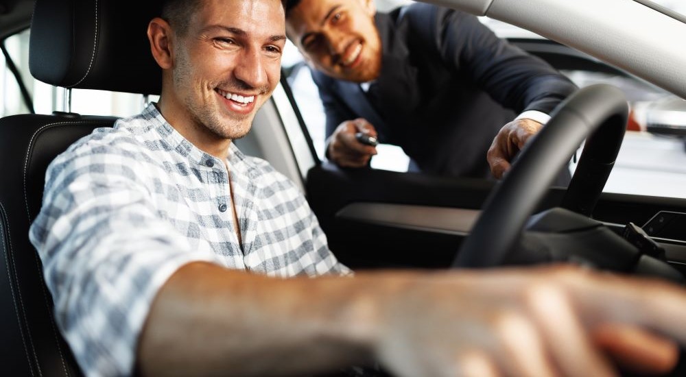 A salesperson and customer are shown smiling at a car dealership.