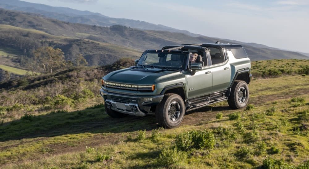 A green 2024 GMC Hummer EV is shown driving on a mountain trail.