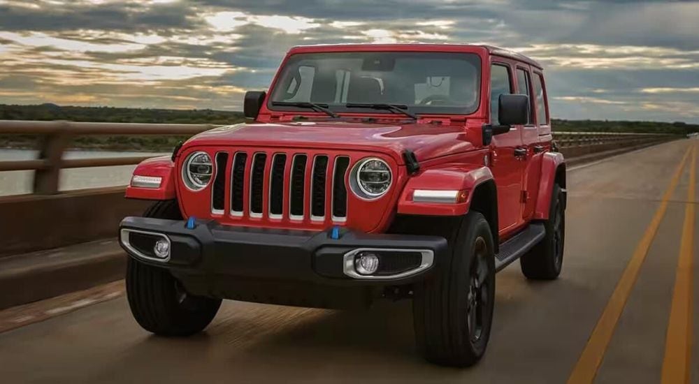 A red 2024 Jeep Wrangler 4xe is shown driving over a bridge.