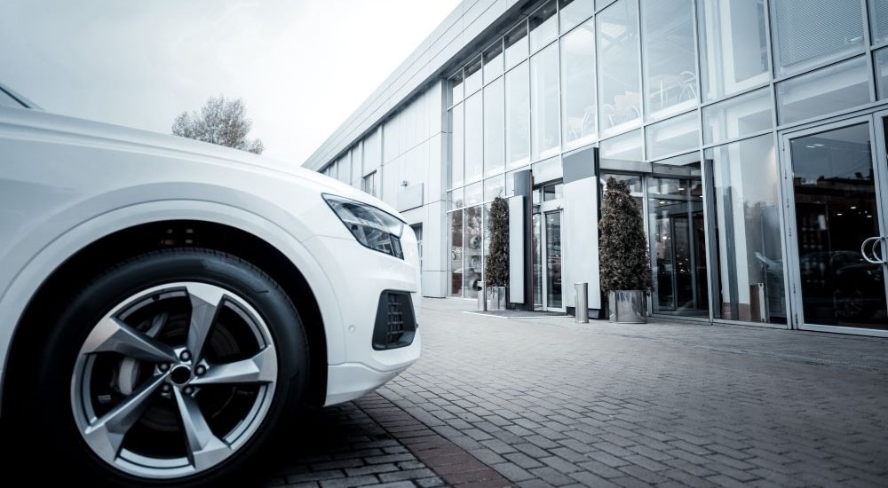 A white car is shown in front of a car dealership.