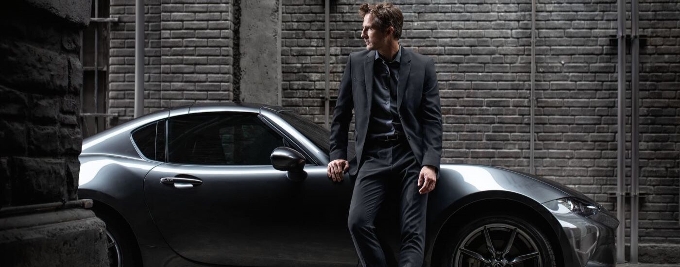 A person is shown leaning against a silver 2022 Mazda MX-5 Miata RF.